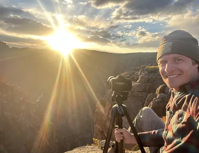 Jordan Grigg with his camera on a tripod at sunrise over a canyon